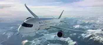 Air Canada airplane flying high in the sky above snow-covered mountains on a clear day.