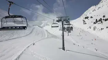 A ski lift carries a group up along a mountainside, allowing them to enjoy the surrounding views of vast snowy slopes and clear blue skies.