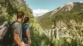 A couple looking out to the Switzerland Landwasser Viaduct, surrounded by lush forests and giant mountains.